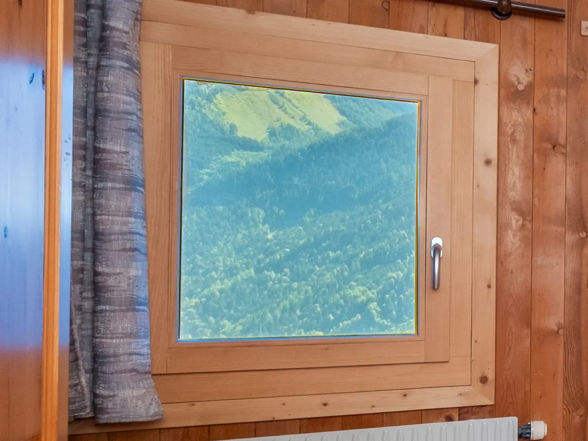 Fenêtre d'un intérieur boisé en contre-jour, donnant sur la montagne en plein soleil, rendu flambient